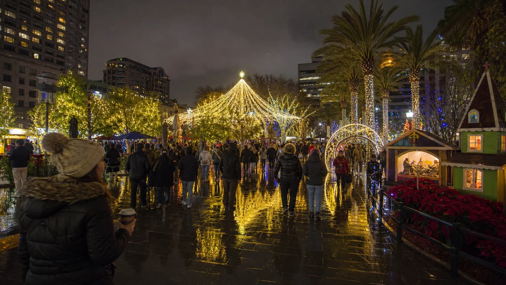 Christmas in the Park visitors in winter coats walking beneath lights reflected on wet San Jose pavement