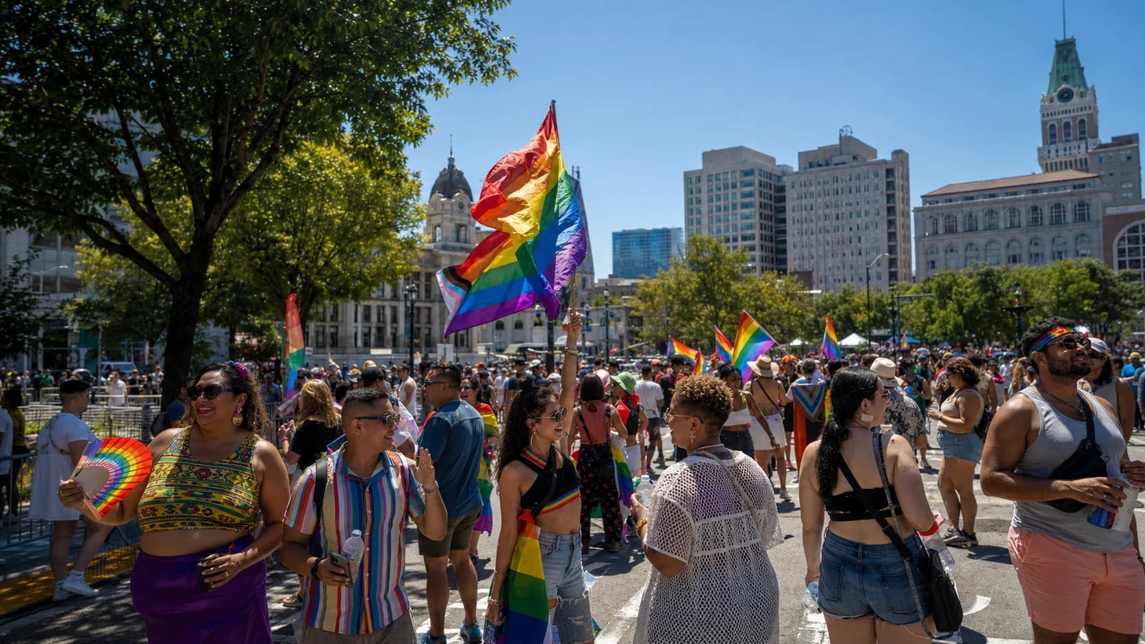 Oakland Pride crowd carrying rainbow flags in bright summer sun near downtown Oakland