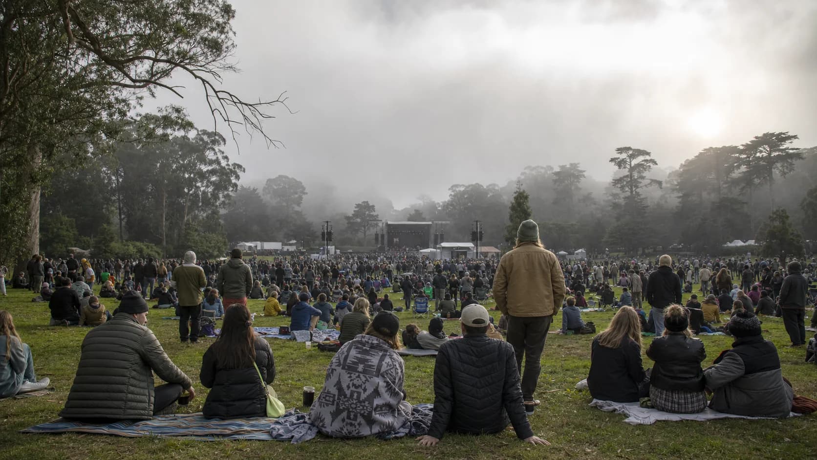 Layered festivalgoers watching a distant stage as low fog drifts through Golden Gate Park