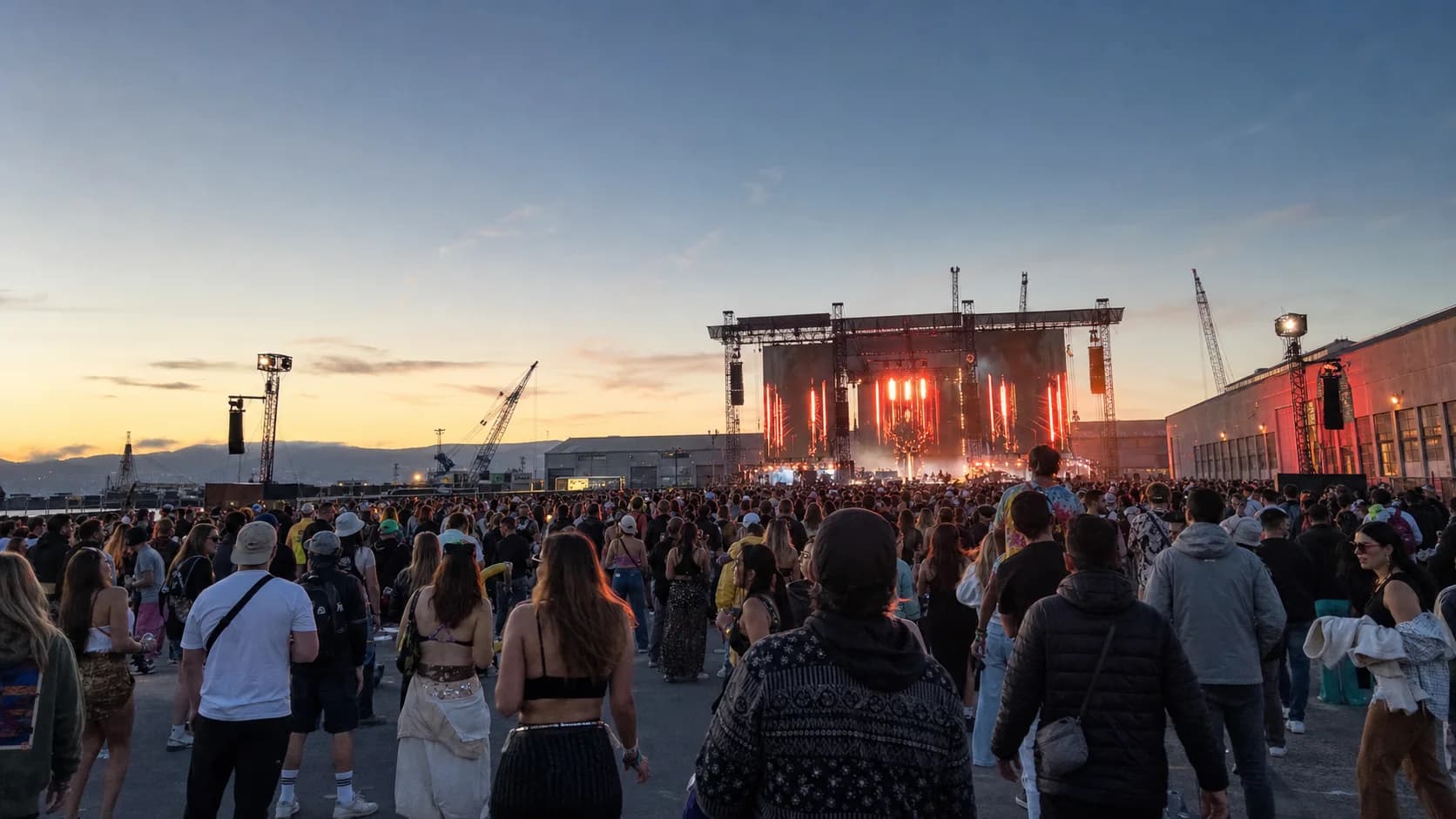 Portola festival crowd facing an outdoor stage at the industrial Pier 80 waterfront near sunset