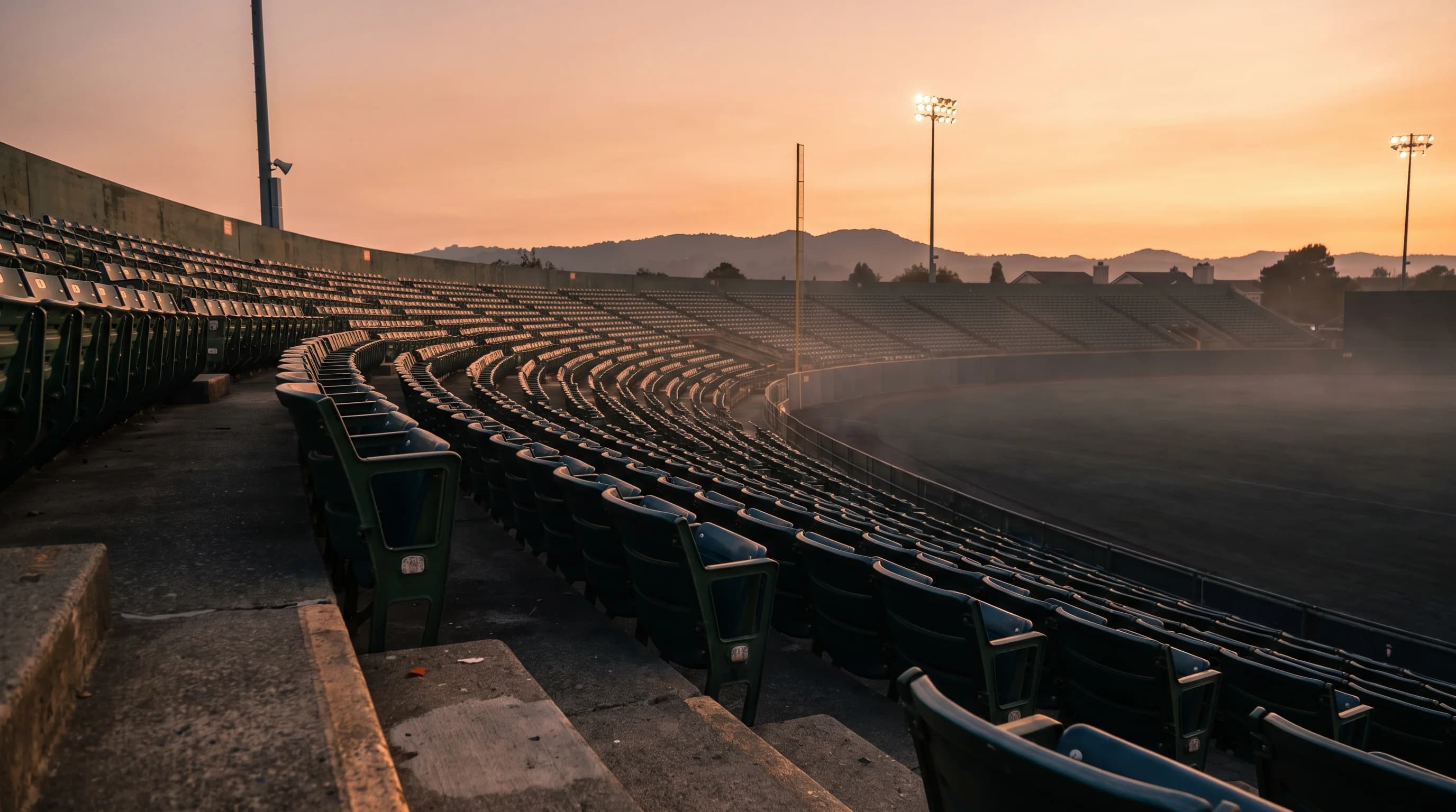 An empty outdoor ballpark seating bowl at dusk on a warm evening