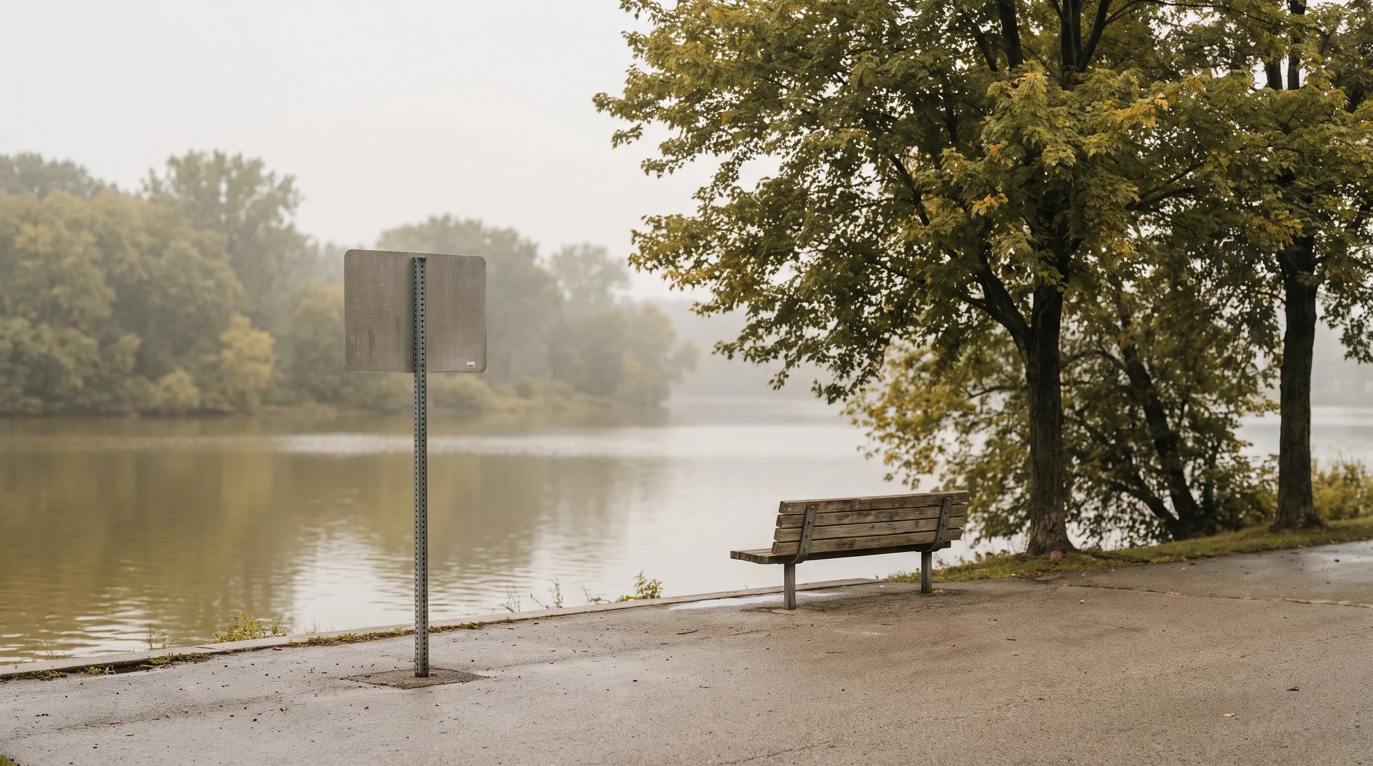 A lakeshore path beside brownish water on a hazy late-summer day